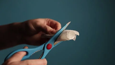 Close-up of hands using blue-handled scissors to cut a piece of white paper Stock Footage 340266188