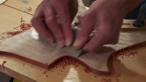 Close-up hands using a cabinet scraper to smooth the edges and guitar top Stock Footage 146960463