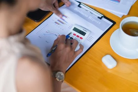 Close-up of hands using calculator on business report with charts beside co.. Stockfoto's
