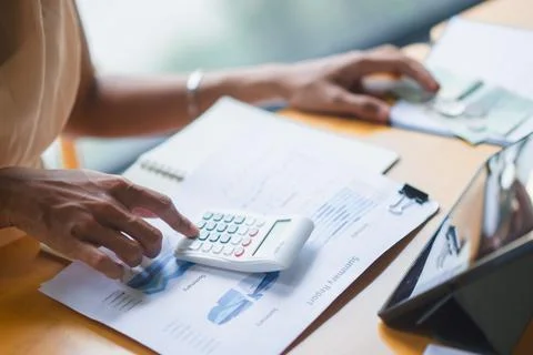 Close-up hands using calculator on summary report beside tablet and coffee,.. Stock Photos