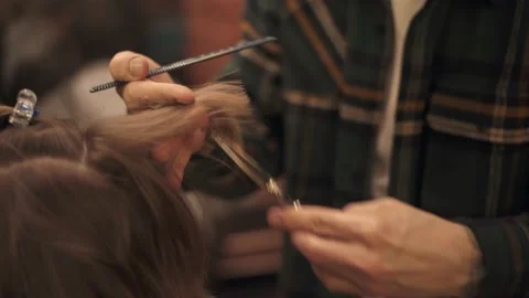 Close-up of hands using comb and scissors while providing a haircut for female Stock Footage 132054042
