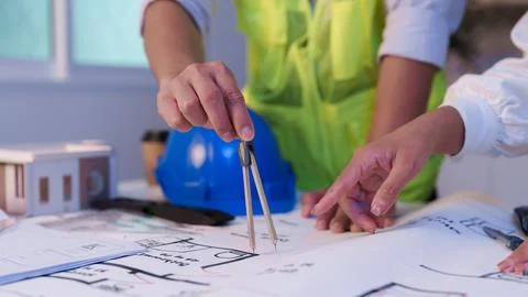 Close up hands using drawing compass on architectural blueprint with hard hat Stock Photos