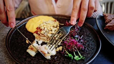 Close up of hands using a fork and knife to cut into a gourmet seared fish Stock Footage 335345872