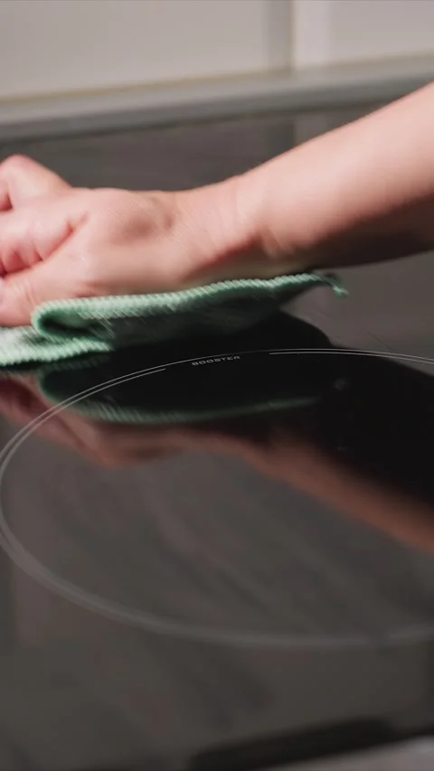 Close up hands using green textured cloth to clean black induction cooktop Stock Footage 345726200