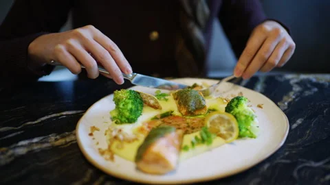Close up of hands using knife and fork to cut a salmon fillet served with 스톡 동영상 329403339