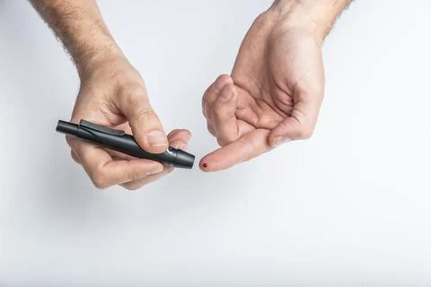 Close up of hands using lancet on finger to check blood sugar level by Glucose Stock Photos