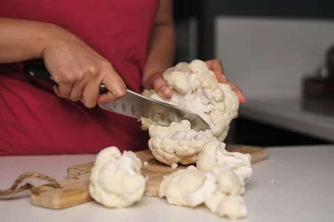 Close-up of hands using a large knife to cut a head of cauliflower on a wooden Foto stock