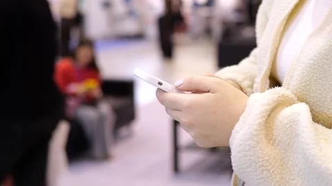 Close-up of hands using mobile phone in busy indoor setting Stock Footage 348992141