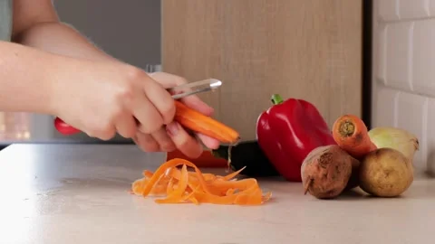 Close-up of hands using a peeler to remove skin from a carrot with bell pep.. Stock Footage 320955789
