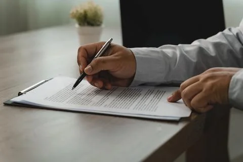 Close-up of hands using a pen to review printed paperwork on a clipboard at.. Stock Photos