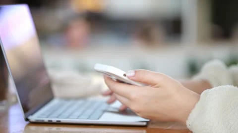 Close-up of hands using phone beside open laptop Stock Footage 345863858