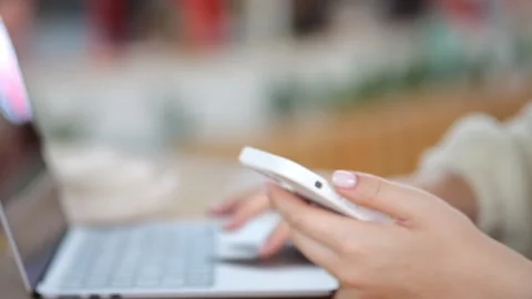 Close-up hands using phone beside open laptop Stock Footage 346216097