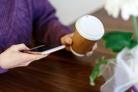 Close up hands using a phone texting on smartphone app and holding paper cup  Foto stock