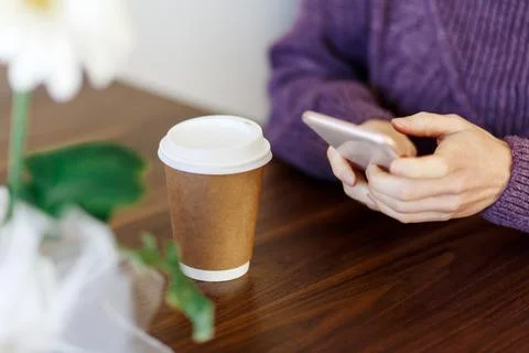 Close up hands using a phone texting on smartphone app and holding paper cup  Foto stock