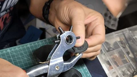 Close up of hands using a rotary punch tool on black leather. Foto stock