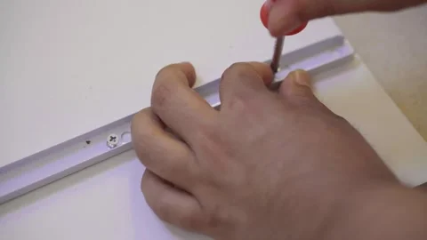 Close-up of hands using a screwdriver to assemble white furniture. 動画素材 323391187