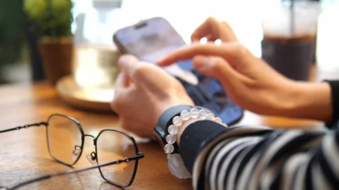 Close-Up Hands Using Smartphone at Café Table with Eyeglasses and Iced Coffee. Stock Footage 322007160