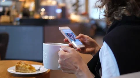 Close up of hands using smartphone in a coffee place and holding white porcelain Stock Footage 150567677