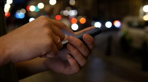Close up of hands using smartphone at night on busy city street, concept of Stock Photos