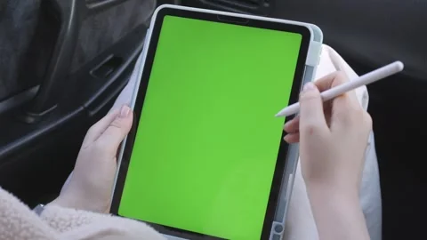 Close-up of hands using stylus on green screen tablet while seated in vehicle Stock Footage 343853224