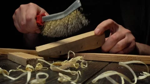 Close-up of hands using a wire brush to smooth wooden planks, with wood shavings Stock Footage 333478260