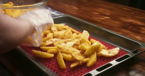 Close up of hands wearing disposable gloves arranging seasoned potato wedges on Video stock 336195047