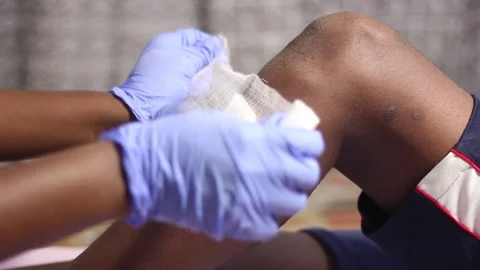 Close up hands wearing gloves wrapping bandage on male leg. injured black man. A Stock-Footage 171167914