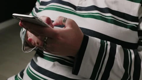Close-up of hands wearing rings and using a smartphone with a striped shirt Stock Footage 339188767