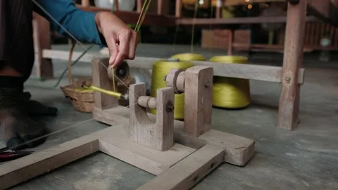 Close up of a hands winding silk thread from a large spool onto a smaller bobbin Stock Footage 325974274