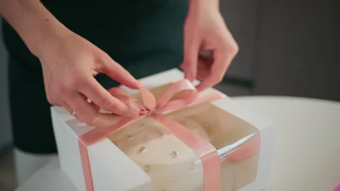 Close-up of hands wrapping a dessert box with a pink ribbon bow 스톡 동영상 336052918