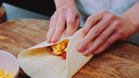 Close-up of hands wrapping a tortilla with egg and cheese indoors Stockbeeldmateriaal 342832832