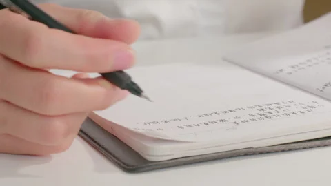 Close-up of Hands Writing Chinese Characters in Notebook on Desk Vidéo 334846891