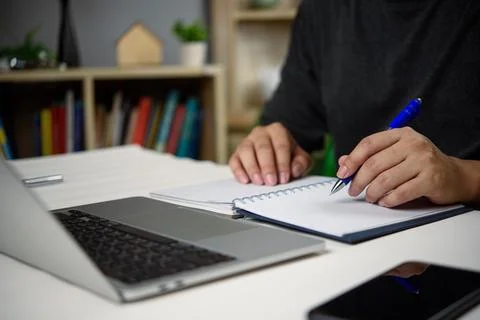 Close-up of hands writing in notebook while working on laptop, and smartpho.. Foto stock