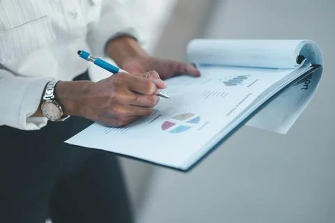 Close-up of hands writing notes on a business summary report with charts an.. Stock Photos