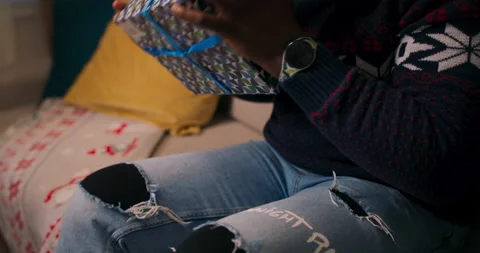 Close-up of the hands of young African-looking guy holding gift and unpacking it Stock Footage 211119577