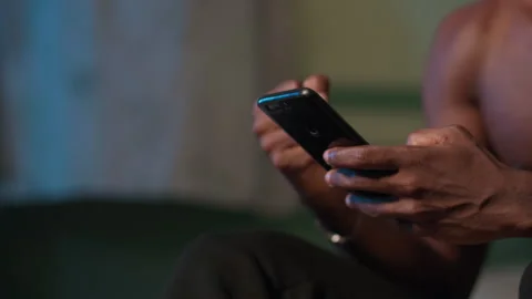 Close-up of hands of young African man holding smartphone. Shows excitement. Video stock 345755778