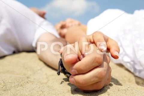 Close-up of hands of young couple lying on sand Stock Photos