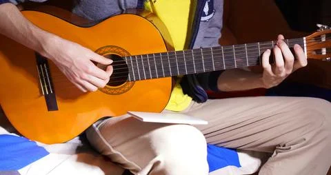 Close-up on the hands of a young man learning a melody on a guitar from not.. 写真素材