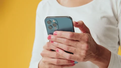 Close-up of hands of young woman using mobile phone isolated on yellow Stockbeeldmateriaal 255964860