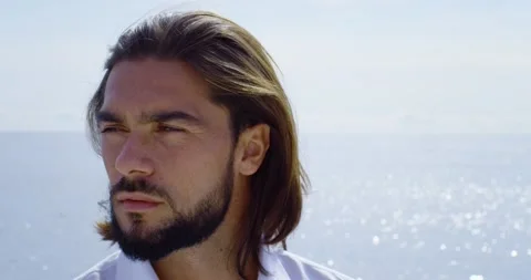 Close-up of a handsome man with a beard and long brown hair. We can see the blue Vídeos de archivo 154693504