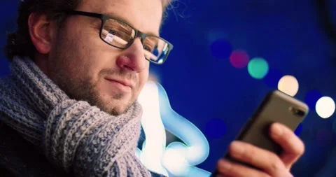 Close up of handsome man with glasses reading message on smartphone standing in Stock Footage 141954124