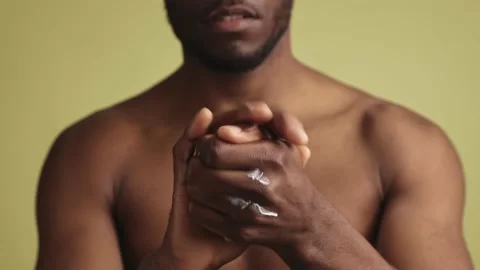 Close-up of handsome sensitive young black man applying hand cream looking at Stock-Footage 233613370