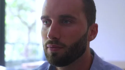 Close-up of a handsome young man with a beard slowly opening his bright blue Vídeos de archivo 344787229