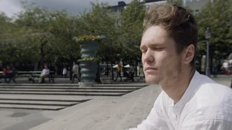 Close up of a handsome young man sitting down in a city square. Vidéo 115983205