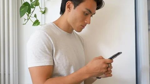 Close-up of handsome young man smiling while using smartphone in house Video stock 114874585