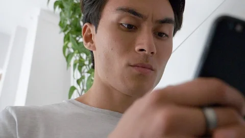 Close-up of handsome young man smiling while using smartphone in house Stock Footage 114874599