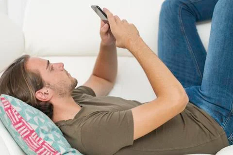 Close up of a handsome young man using his phone while lying on a sofa. Relax Stock Photos