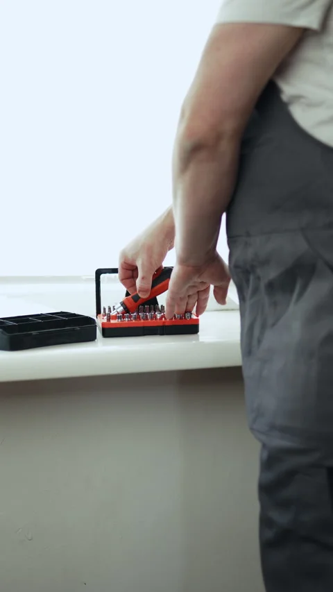 Close-up of a handyman in a jumpsuit assembling a multi-bit screwdriver, profess Видео 335644157