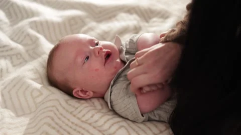 Close-up of a happy baby lying on a patterned blanket while a parent gently Video stock 340636977
