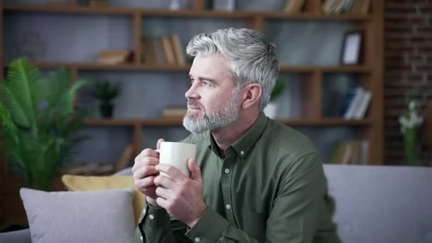 Close up of happy bearded man with gray hair sitting on sofa at home holding  Stock Footage 328706393